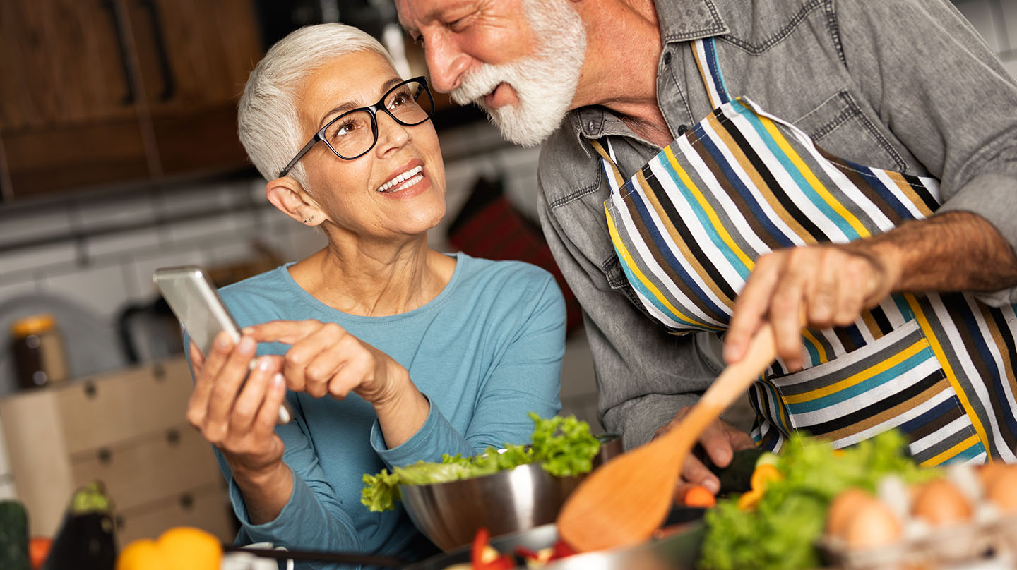 Gesund abnehmen: Älteres Pärchen beim Kochen in der Küche, im Vordergrund eine Salatschüssel.