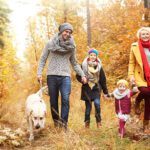 Herbstblues: Junge Familie mit zwei kleinen Kindern und Hund spazieren gut gelaunt durch den Herbstwald.